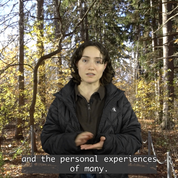Young woman with wavy brown, shoulderlength hair, wearing a black puffer jacket, standing in a forest. subtitles read, "and the personal experiences of many."